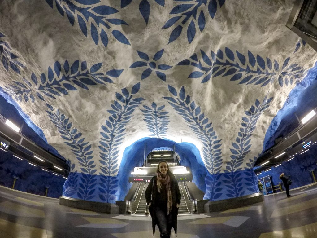 Rachel na estação de metrô de Estocolmo com pinturas de folhas azuis nas paredes de pedra.